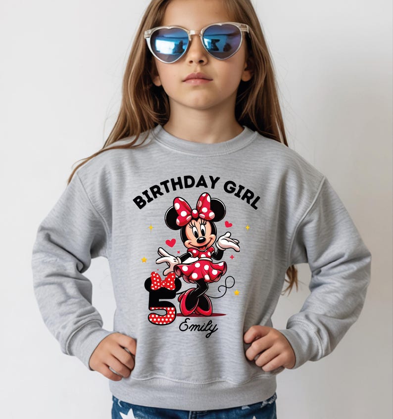 A young girl wearing a gray sweatshirt with a Minnie Mouse design and sunglasses, celebrating her 5th birthday.