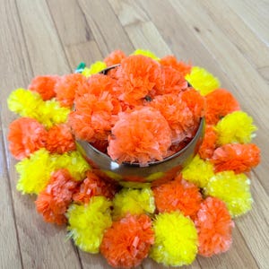 May include: A bowl filled with orange and yellow paper flowers, arranged in a circular pattern on a wooden surface.
