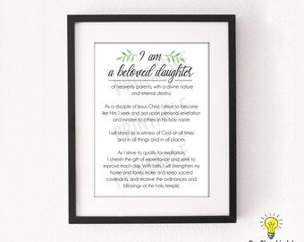 Könnte beinhalten: Gerahmter Druck mit dem Text "I am a beloved daughter" in dekorativer Schrift, mit schwarzem Rahmen und weißem Passepartout. Der Druck enthält eine religiöse Botschaft und ist für die Heimdekoration geeignet.