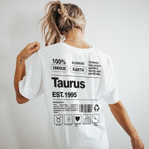May include: White t-shirt with the word "Taurus" in bold black letters. The shirt features additional text including "100% Unique", "Element Earth", and "EST. 1995". Below the text are icons and the words "The Bull", "Intelligent", "Made with Love", and "Hardworking".
