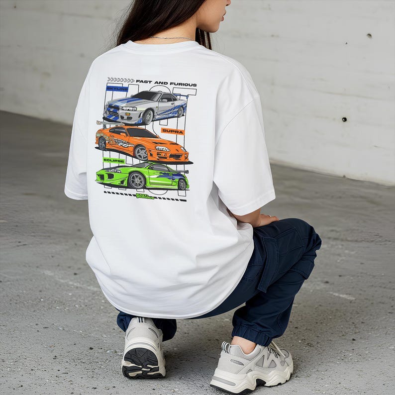May include: White t-shirt featuring three stylized race cars in blue, orange, and green, with the text "FAST AND FURIOUS" above. The cars are labeled "SUPRA" and "ECLIPSE".