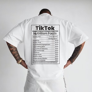 May include: White short-sleeved t-shirt with a graphic on the back that reads "TikTok Nutrition Facts." The graphic lists various metrics such as creativity, screen time, and social media engagement, with corresponding percentage values.