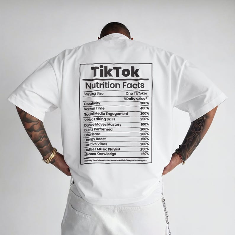 May include: White short-sleeved t-shirt with a graphic on the back that reads "TikTok Nutrition Facts." The graphic lists various metrics such as creativity, screen time, and social media engagement, with corresponding percentage values.