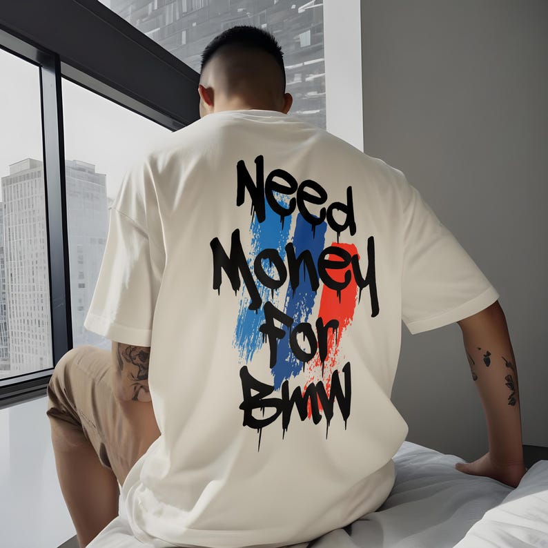 May include: A white t-shirt with the text "Need Money For BMW" in black, with blue and red brushstroke accents. The shirt is a casual style.