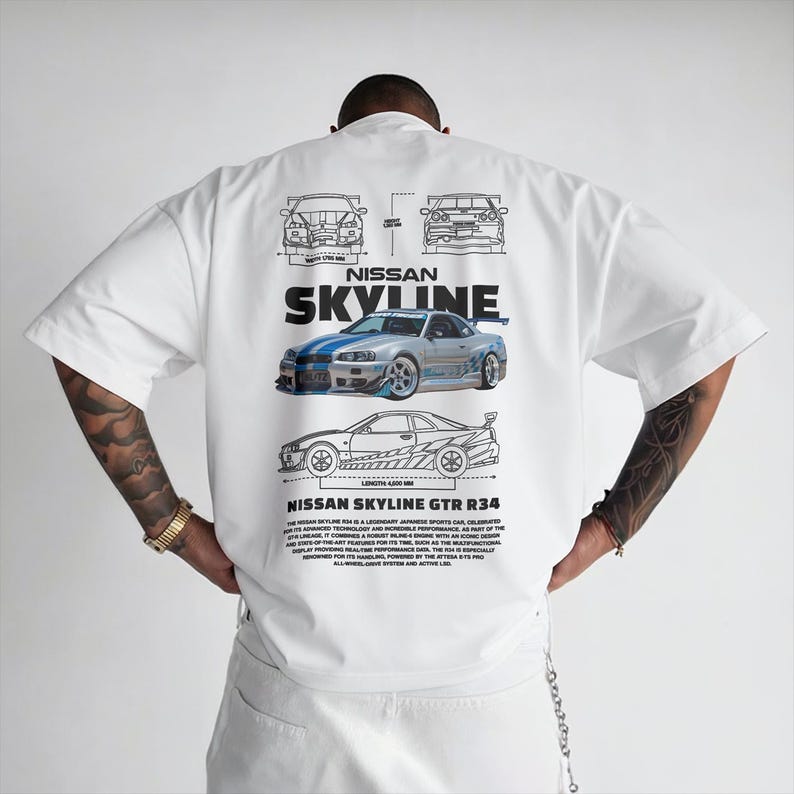 May include: White short-sleeve t-shirt featuring a graphic of a silver and blue Nissan Skyline GTR R34 car. The design includes blueprints and text that reads "NISSAN SKYLINE GTR R34".