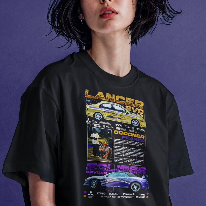 May include: Black t-shirt featuring a graphic design with two race cars, a yellow Lancer Evo and a purple Eclipse Spyder. The shirt includes text with car details and sponsor logos.