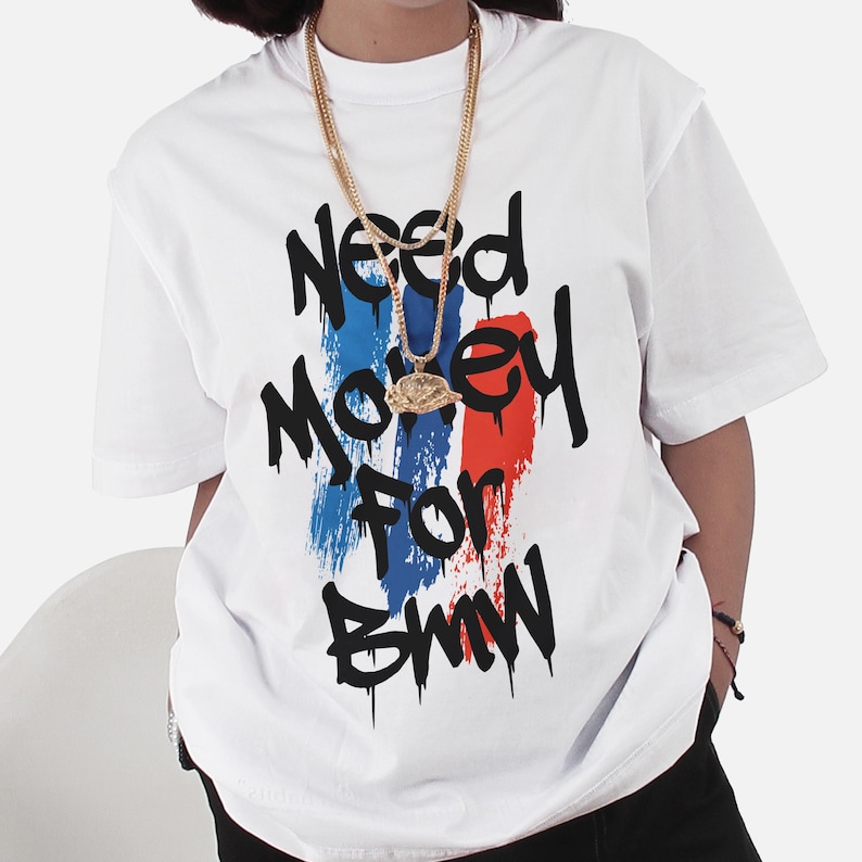 May include: White t-shirt with the text "Need Money For BMW" in black dripping font. The text is over a vertical stripe design in blue, red, and white. A gold chain necklace is worn over the shirt.