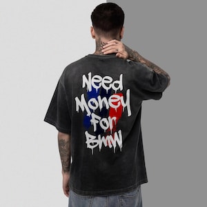 May include: Dark gray t-shirt with the text "Need Money For BMW" in white, with blue and red vertical stripes. The shirt has a vintage, washed-out look.