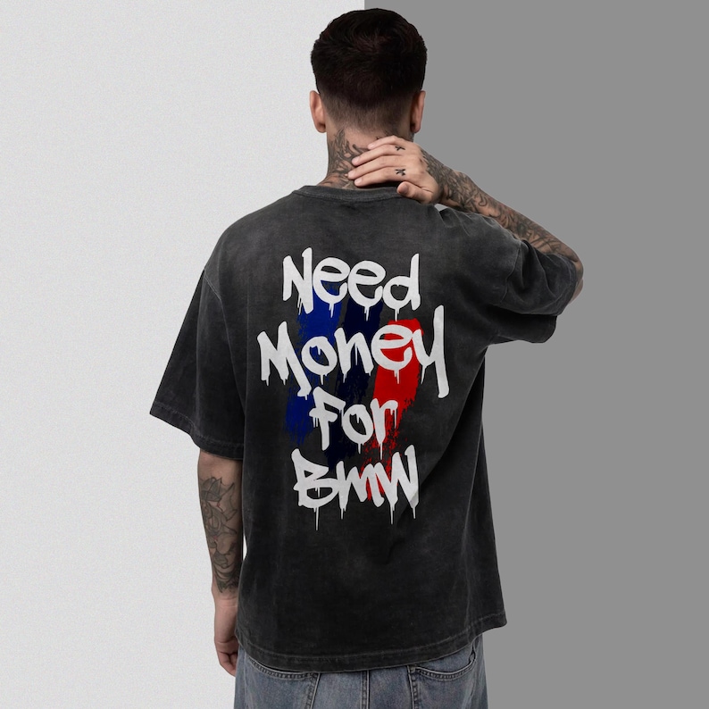 May include: Dark gray t-shirt with the text "Need Money For BMW" in white, with blue and red vertical stripes. The shirt has a vintage, washed-out look.