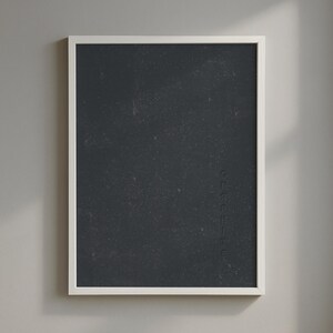 Puede incluir: Una obra de arte enmarcada con una superficie texturizada de color gris oscuro. La obra de arte está encerrada en un marco rectangular blanco. Se puede ver un texto tenue en el lado derecho de la obra de arte. La obra de arte se exhibe contra una pared gris claro.
