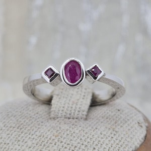Peut inclure: Bague en argent ornée d'un rubis central ovale et de deux rubis carrés. La bague présente une monture texturée et un design simple et élégant. Les rubis sont d'un rouge profond.
