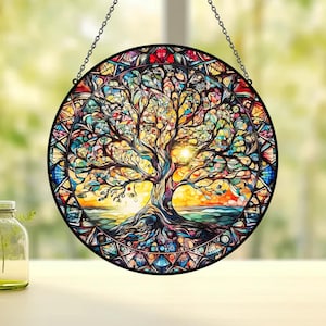 Peut inclure: Une fenêtre en vitrail suspendue avec un motif coloré d'arbre de vie. L'arbre a un tronc épais et de nombreuses branches avec des feuilles dans des tons de vert, jaune, orange, rouge et bleu. L'arrière-plan est une scène de coucher de soleil avec un ciel bleu et des nuages orange.