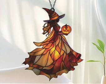 May include: A stained glass suncatcher featuring a witch wearing a pointed hat and a flowing gown made of orange, yellow, and red glass segments. The witch holds a glowing orange jack-o'-lantern pumpkin. The piece hangs from a silver chain.