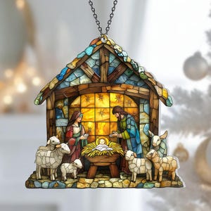 May include: A stained-glass style Christmas ornament depicting the Nativity scene. The ornament features Mary, Joseph, baby Jesus, sheep, and a stable. The ornament is suspended by a silver chain.