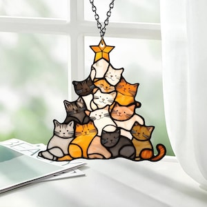 May include: A stained glass Christmas tree ornament featuring a stack of cats in various colors, including white, orange, black, and gray. The cats are arranged in a pyramid shape with a star on top.