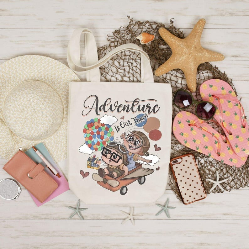 Puede incluir: Un bolso tote crema con la frase "Adventure Is Out There" y una ilustraci&oacute;n de dibujos animados de dos personajes en un avi&oacute;n con globos. La imagen tambi&eacute;n incluye un sombrero de paja, gafas de sol, chanclas rosas y una estrella de mar.
