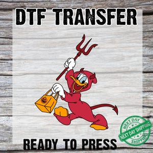 May include: DTF transfer graphic featuring a cartoon duck dressed as a devil, holding a trident and a pumpkin-shaped bag. The text "DTF TRANSFER" and "READY TO PRESS" are displayed above and below the image, with a "NEXT DAY SHIPPING" stamp.