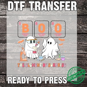 May include: DTF transfer design featuring ghosts in a lab setting. The design spells "BOO" using elements from the periodic table. The phrase "THE ELEMENT OF SURPRISE" is below the ghosts, and "READY TO PRESS" is at the bottom.