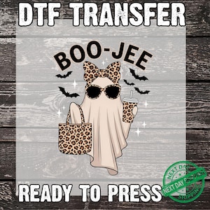 May include: A DTF transfer design featuring a cartoon ghost wearing sunglasses, a bow, and holding a leopard print tote bag and a coffee cup. The text "BOO-JEE" and "READY TO PRESS" are included in the design. Black bats are also included.