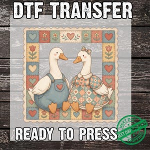 May include: A DTF transfer ready to press featuring two illustrated ducks inside a patchwork border. One duck wears blue overalls, the other a checkered dress with a bow. The border contains hearts and flowers in muted tones of red, blue, and yellow.