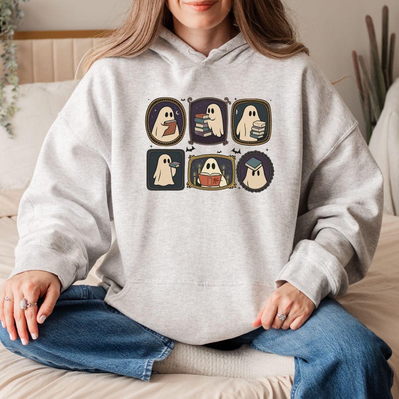 May include: Light grey hoodie with a rectangular graphic showcasing six framed illustrations of cartoon ghosts reading books. The ghosts are in different poses, holding books, and wearing a graduation cap. The design has a vintage, retro aesthetic.