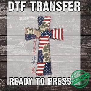 May include: DTF transfer featuring a cross design with a patchwork of American flag and camouflage patterns. The words "god bless america" are written vertically on the left side of the cross. The words "READY TO PRESS" are at the bottom.