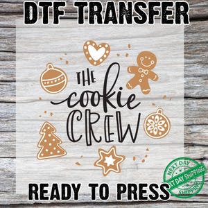 May include: A DTF transfer design featuring the text "THE cookie CREW" with gingerbread man, heart, star, Christmas tree, and ornament illustrations. The words "READY TO PRESS" are also included.