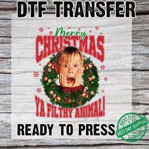 以下が含まれることがあります： DTF転写。驚いた表情の子供がクリスマスのリースに囲まれています。「Merry Christmas」、「Ya Filthy Animal!」、および「Ready to Press」のテキストが含まれています。