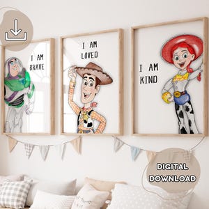 May include: Three framed prints featuring Toy Story characters: Buzz Lightyear, Woody, and Jessie. Each print has a character and a positive affirmation: "I AM BRAVE", "I AM LOVED", and "I AM KIND". The prints are displayed above a row of pillows.