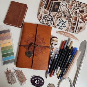May include: A collection of stationery items including a brown leather-bound journal with a butterfly design, a zippered pouch with owl and potion illustrations, various pens, markers, stickers with potion labels, a beaded bracelet, and sticky tabs.