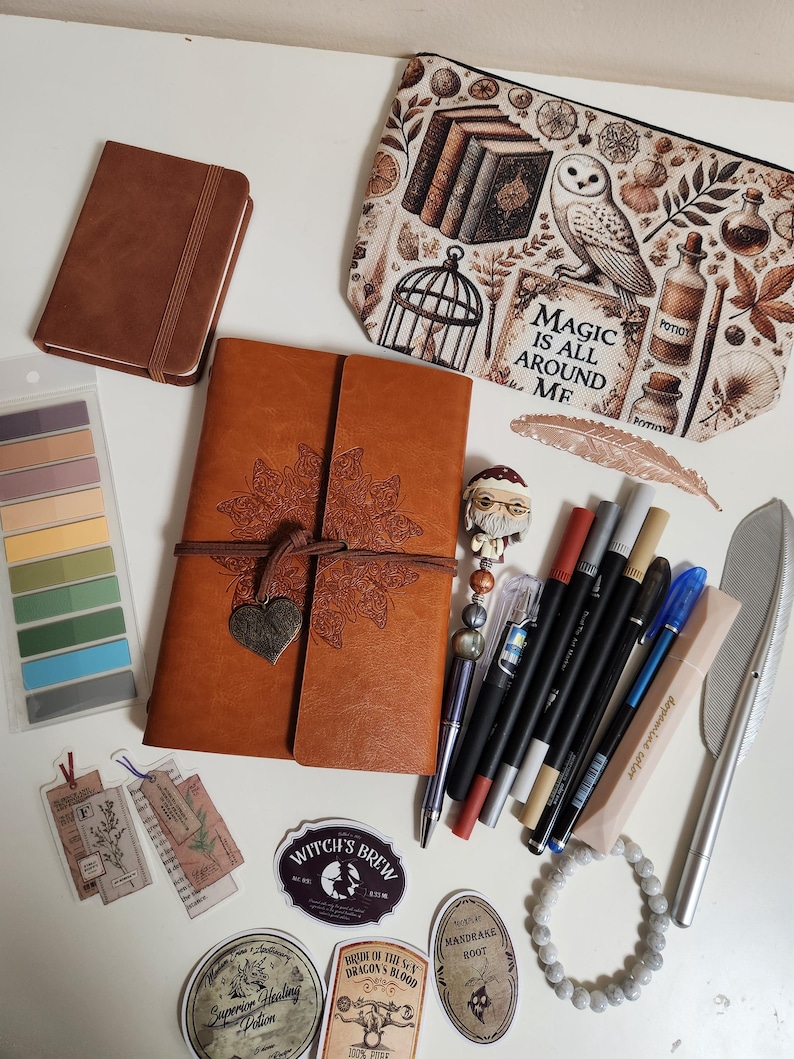 May include: A collection of stationery items including a brown leather-bound journal with a butterfly design, a zippered pouch with owl and potion illustrations, various pens, markers, stickers with potion labels, a beaded bracelet, and sticky tabs.