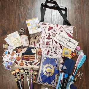 May include: A collection of Harry Potter themed merchandise including a tote bag with a pattern of magical items, a blue lockable journal, a snow globe box, a wooden sign reading Restricted Section Do Not Enter, various pens with character toppers, stickers, and stationery.