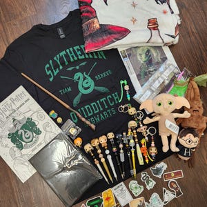 Peut inclure: Une collection d'objets sur le thème d'Harry Potter comprenant un t-shirt noir de Quidditch Serpentard, une couverture à motifs, un livre de coloriage, une baguette, plusieurs stylos personnages, une peluche Dobby, des autocollants et divers accessoires.