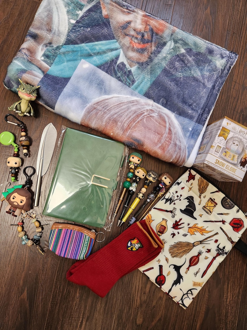 May include: A collection of merchandise including a printed fleece blanket, a green notebook, a snow globe box, a red sock with a crest, a patterned pouch, a small coin purse, four character pens, a metal letter opener, and several keychains.