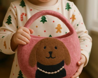 Könnte beinhalten: Eine rosa Filzhandtasche mit einem braunen Hundeapplikation. Der Hund hat einen schwarzen Kragen mit weißen Nähten. Die Tasche hat einen abgerundeten Griff und wird von einer Person gehalten, die ein cremefarbenes Hemd mit Weihnachtsmustern trägt.