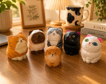 Könnte beinhalten: Eine Sammlung von sechs kleinen, handgeschnitzten Tierfiguren aus Holz. Das Set besteht aus fünf Katzen mit unterschiedlichen Farbmustern—orange getigert, braun, grau getigert, schwarz und weiß—sowie einem kleinen hellbraunen Hund in der Mitte.