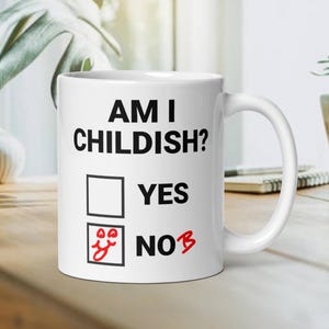 Könnte beinhalten: Weiße Keramiktasse mit schwarzem Text, der "Bin ich kindisch?" lautet, mit einem Kontrollkästchen neben den Wörtern "Ja" und "Nein". Das Kästchen "Nein" ist mit einem roten Smiley angekreuzt.