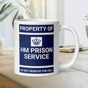 Könnte beinhalten: Eine weiße Keramiktasse mit einem blau-weißen Design. Die Tasse trägt die Aufschrift "Property of HM Prison Service" und "Do Not Remove For Cell".