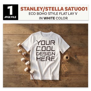 May include: White t-shirt with the text "YOUR COOL DESIGN HERE" in black block letters. The shirt is laid flat on a wooden surface, with cotton stems, a ball of twine, and a tag. The image also includes text that says "STANLEY/STELLA SATU001 ECO BOHO STYLE FLAT LAY V IN WHITE COLOR".