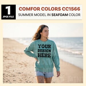 May include: A person wearing a seafoam green sweatshirt with the text "YOUR DESIGN HERE" in black block letters. The sweatshirt is paired with denim shorts. The image includes the text "COMFOR COLORS CC1566 SUMMER MODEL IN SEAFOAM COLOR".
