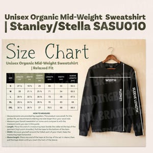 Może przedstawiać: Czarna bluza Unisex Organic Mid-Weight Sweatshirt wisi na drewnianym wieszaku. Obraz zawiera tabelę rozmiarów z wymiarami w cm dla rozmiarów S, M, L, XL i 2XL. Tekst na obrazie brzmi "Unisex Organic Mid-Weight Sweatshirt | Stanley/Stella SASU010".