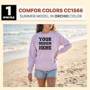 May include: A light purple sweatshirt with the text "YOUR DESIGN HERE" in black. The sweatshirt is part of the "COMFOR COLORS CC1566 SUMMER MODEL IN ORCHID COLOR" collection. The model is wearing denim shorts and standing on a beach.