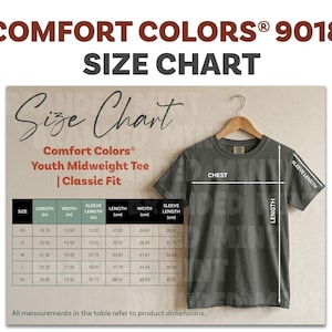 May include: A size chart for Comfort Colors Youth Midweight Tee, Classic Fit. The chart includes measurements for chest, length, and sleeve length in inches, with sizes ranging from XS to XL. The shirt is displayed on a wooden hanger.