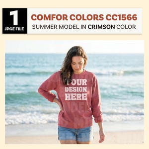 May include: A woman wearing a crimson-colored sweatshirt and denim shorts stands on a beach. The sweatshirt has the text "YOUR DESIGN HERE" in white. The image is labeled "COMFOR COLORS CC1566 SUMMER MODEL IN CRIMSON COLOR."