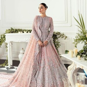 May include: A long, flowing pink gown with intricate silver embroidery and a matching sheer dupatta. The gown has a fitted bodice and a full skirt.