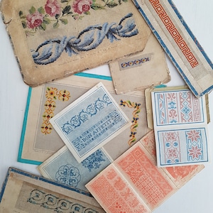 Könnte beinhalten: Sortiment an Vintage-Stickmustern auf Papier. Die Muster umfassen ein blaues und weißes Blumenmuster, ein rotes und weißes geometrisches Muster und ein blaues und weißes Muster mit dem Text "Guten Appetit".