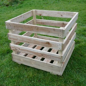 Peut inclure: Caisse en bois carrée, ouverte sur le dessus, faite de planches de couleur claire. La caisse a une base et des côtés à lattes, et est posée sur de l'herbe verte. Idéale pour le jardinage ou le stockage.