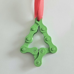 Puede incluir: Adorno navideño verde con forma de árbol, hecho con una cadena de bicicleta. Colgante de una cinta roja, este adorno original es una decoración ecológica para las fiestas.