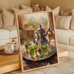 Könnte beinhalten: Aquarellmalerei einer silbernen Teekanne und Gläsern Tee mit Minze auf einem dekorativen Tablett. Das Bild ist in einem hellen Holzrahmen gerahmt und steht auf einem Holztisch. Der Hintergrund zeigt ein Fenster und ein Sofa mit Kissen.