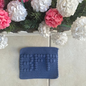May include: A blue crocheted square with a textured pattern. The square has a raised design that resembles the letters "DIY".